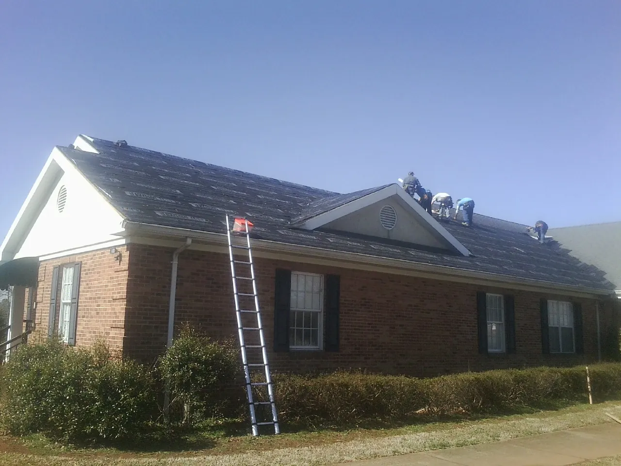 Crew tearing shingles off a brick ranch roof with a ladder set — Metal Roof Repair work by our crew in Fairchance