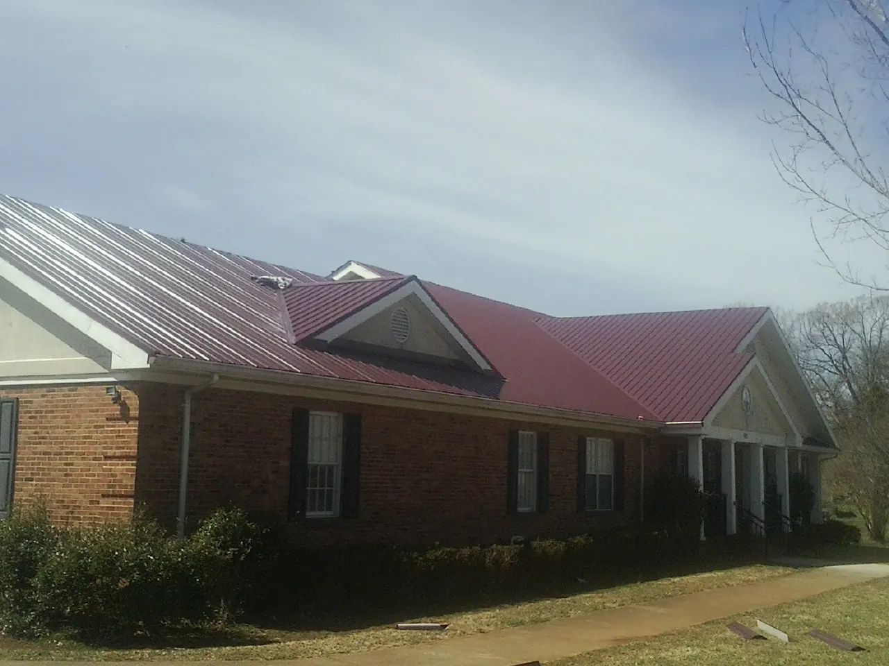Red metal roof with gabled entries on a long brick building, from a Hail Damage Roof Repair job in Fairchance
