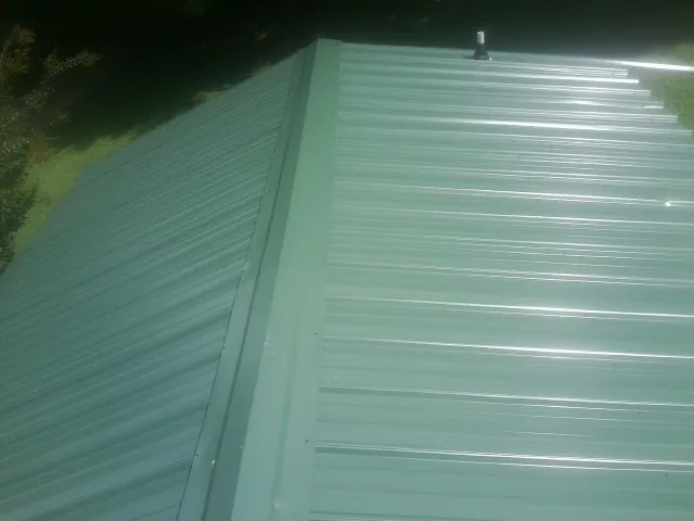 New green metal panels meeting at the ridge of a roof — Flat Roof Repair work by our crew in Fairchance