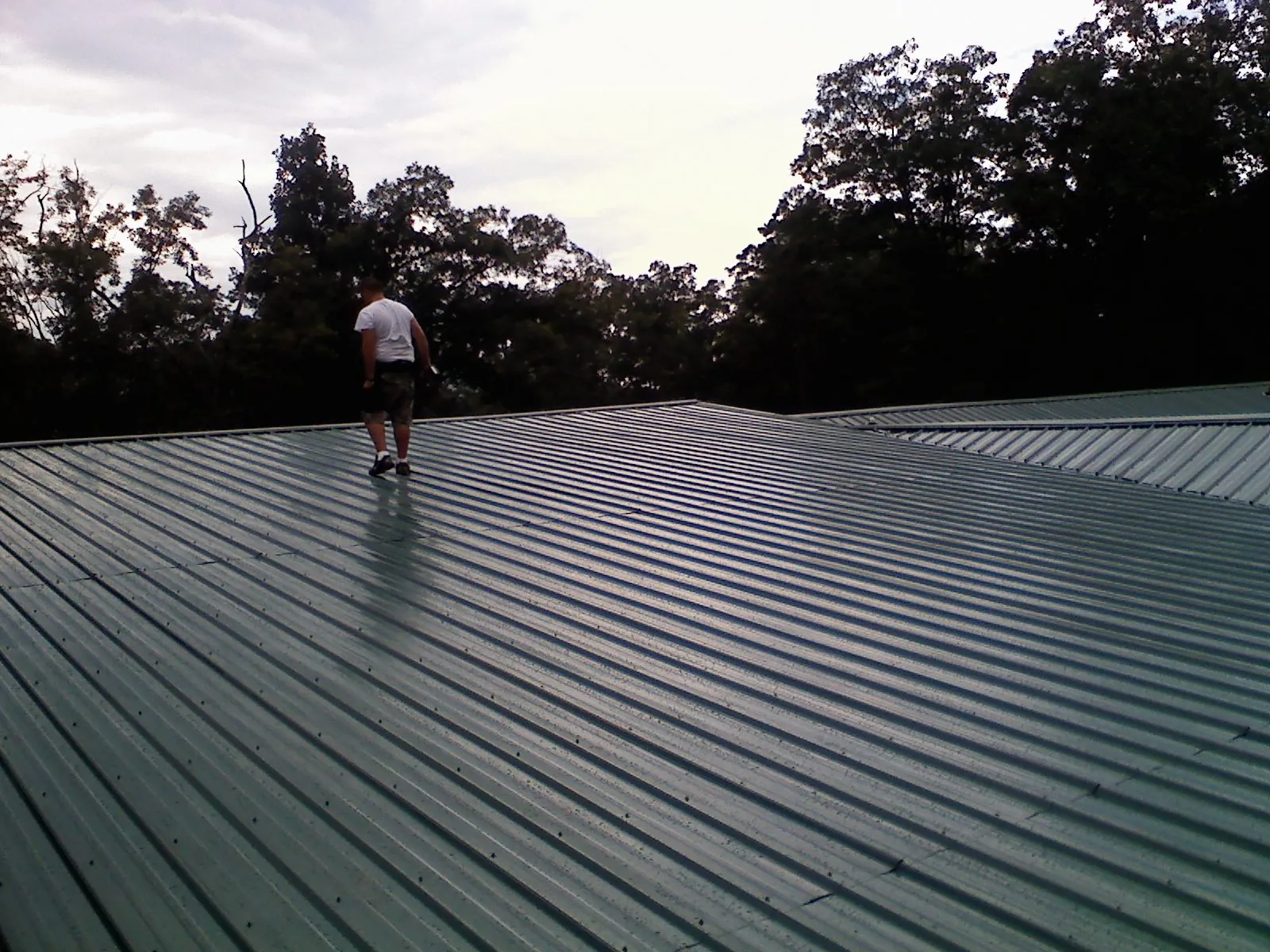 Roofer walking a wide expanse of new green metal roofing in Fairchance
