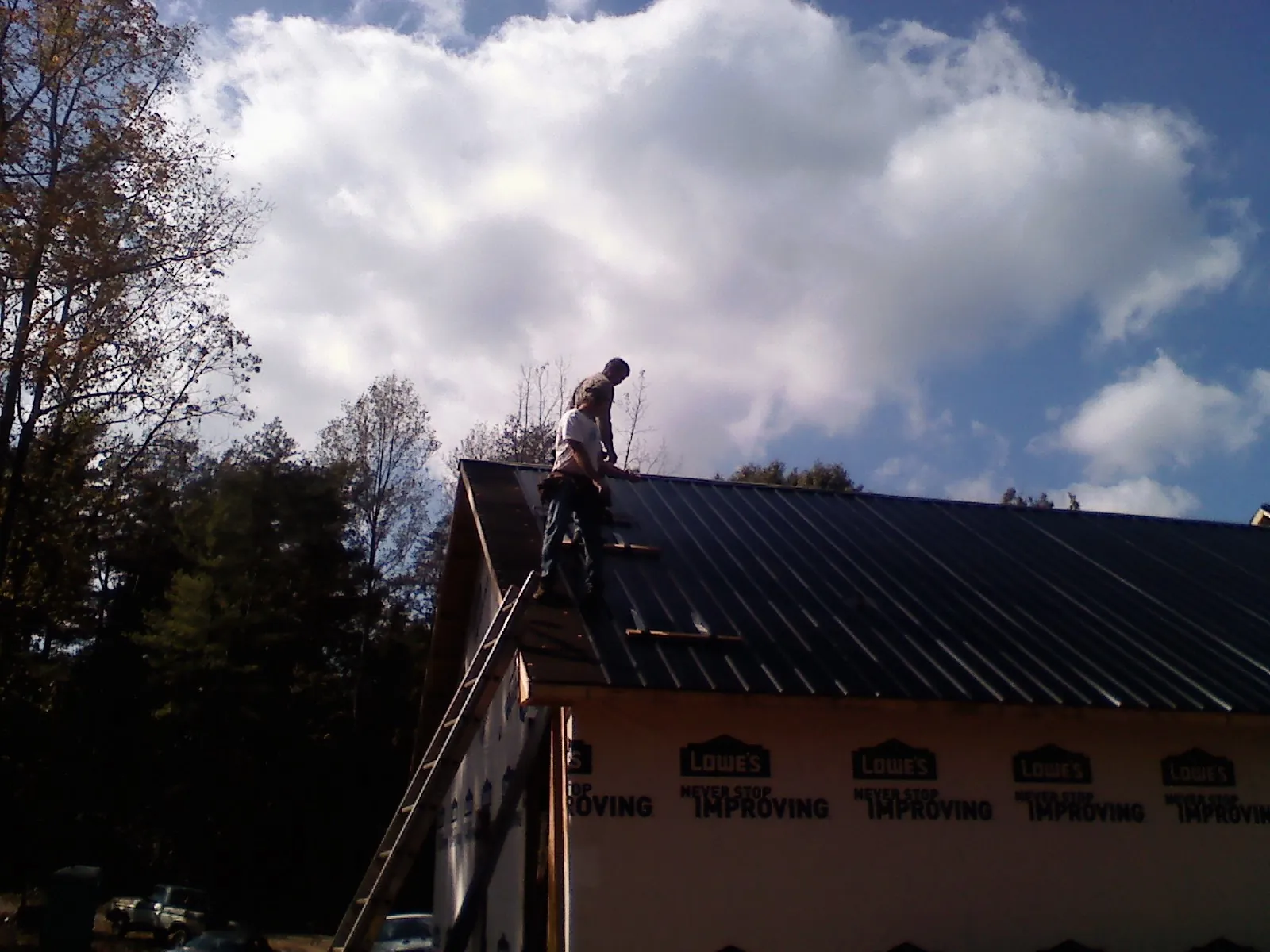 Roofer fastening dark metal panels high against a cloudy sky, from a Roof Inspection job in Fairchance