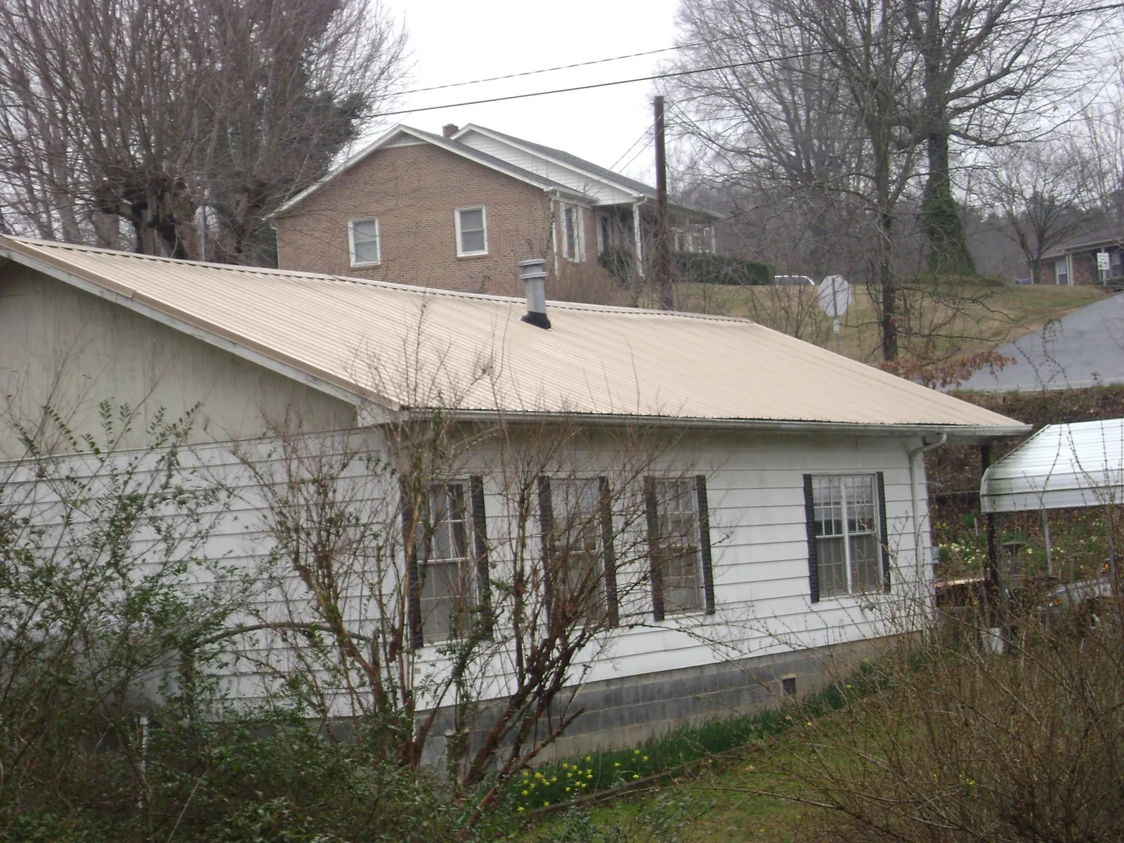 Tan metal roof on a white sided house set into a hillside — Commercial Roofing by Roofing Brothers in Fairchance