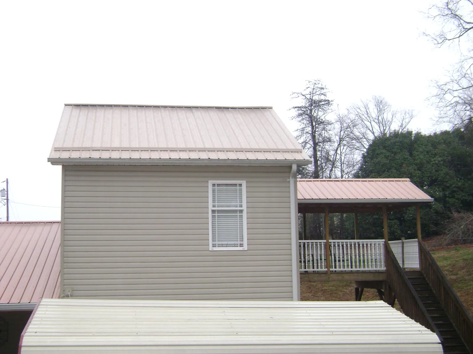 Tan metal roofs on a two story addition and attached porch, from a Roof Replacement job in Fairchance
